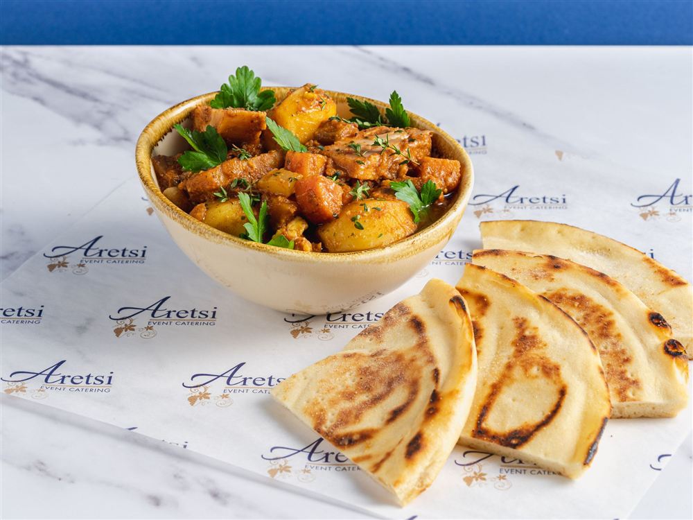 A bowl of Aretsi slow-cooked stew with potatoes and parsley, with warm pitta