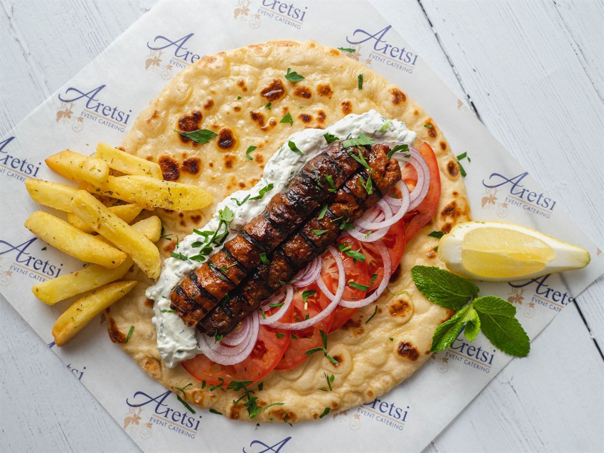 An open Aretsi kebab pitta with tzatziki, tomato, red onion, fries, lemon and mint