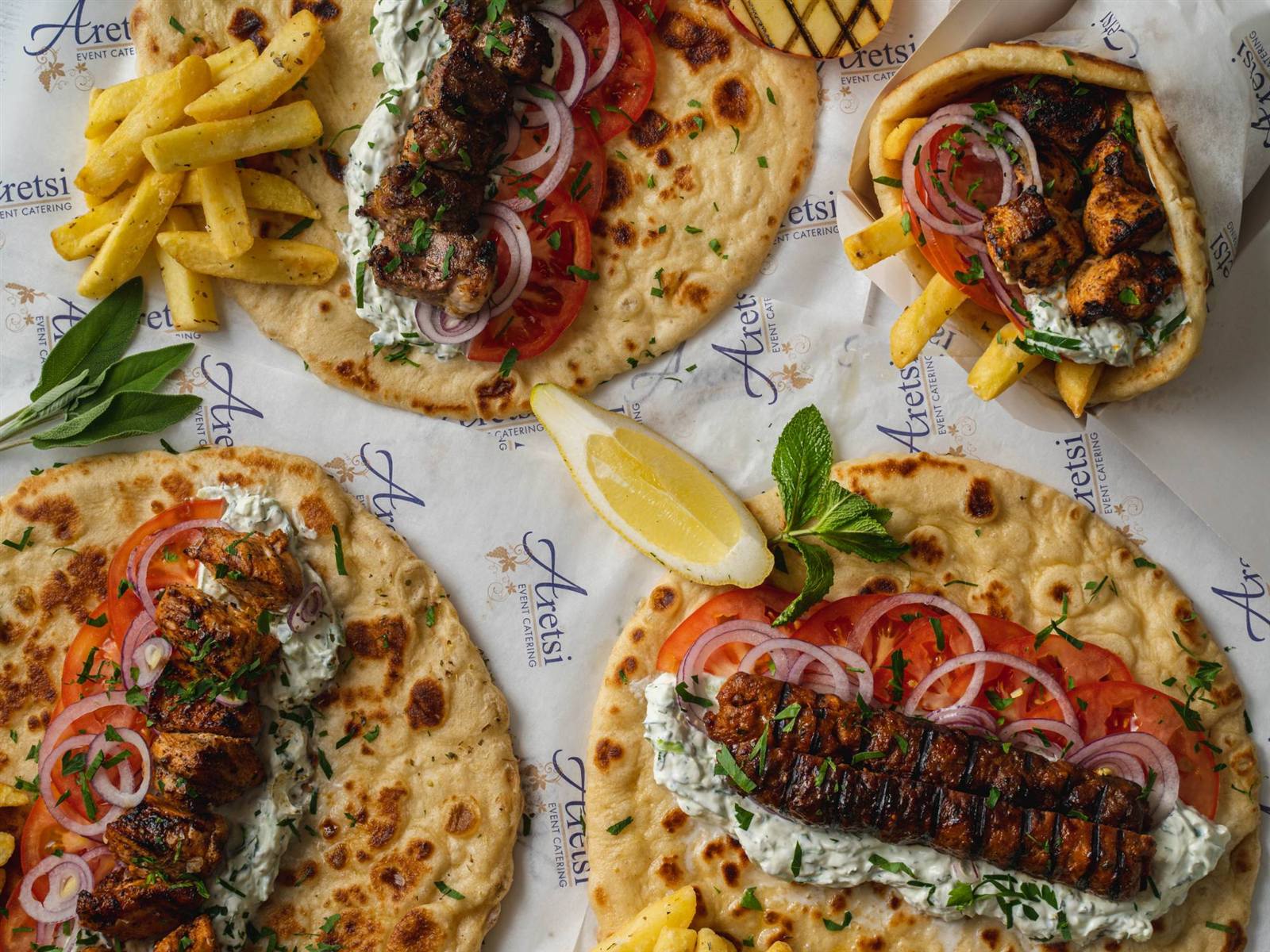 Four Aretsi pittas, open and wrapped, with souvlaki, kebab, fries and tzatziki on Aretsi paper