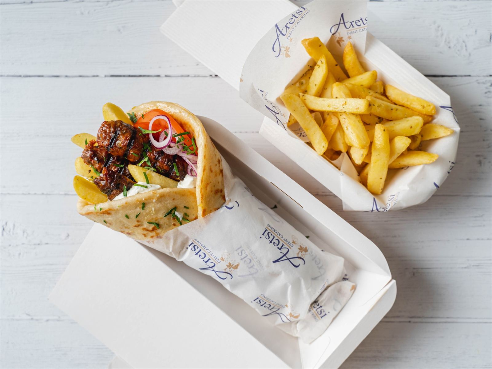 An Aretsi pork souvlaki pitta in a branded box beside a box of oregano fries